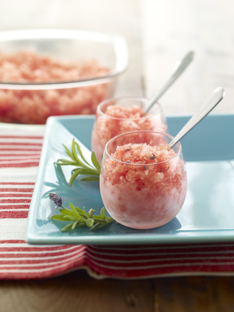 Lavender Sorbet or Granita served in two clear glass dessert dishes garnished with sprigs of lavender. Serving bowl full of Sorbet/Granita in background.