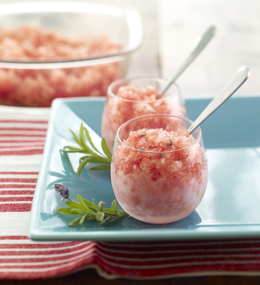 Lavender Sorbet or Granita served in two clear glass dessert dishes garnished with sprigs of lavender. Serving bowl full of Sorbet/Granita in background.