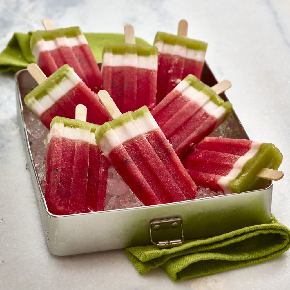 Eight Layered Watermelon Popsicles set in metal tray with crushed ice. Green cloth napkin in background.