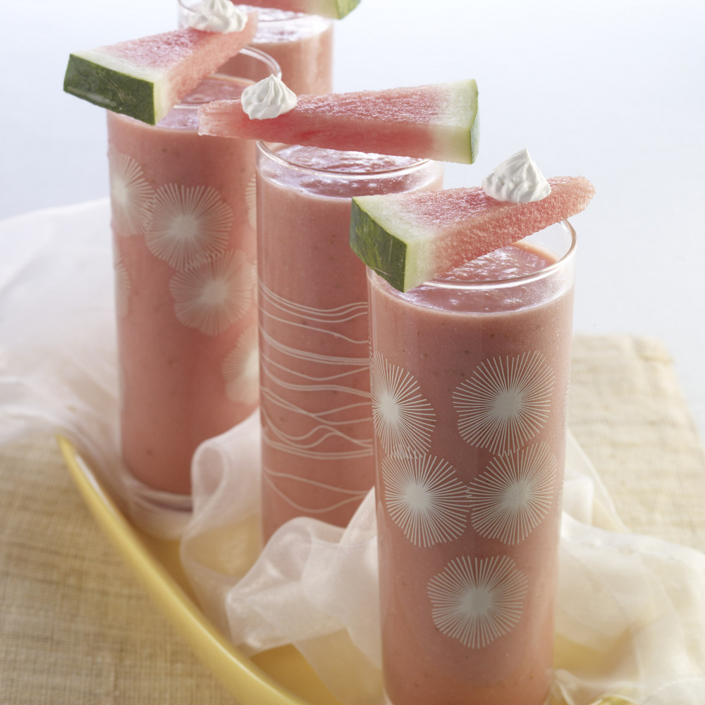 Three Watermelon Malibu Cocktails served in tall decorative glasses, garnished with thin triangular watermelon cuts with small amount of whipped topping. Served on yellow serving tray.