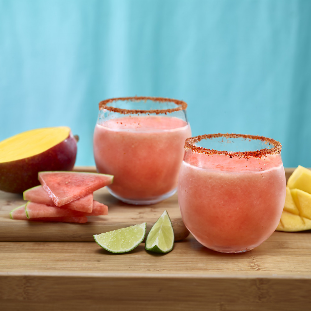 Watermelon Mango Margaritas in Tajin spice rimmed glasses. Garnishes of watermelon, mango and lime.