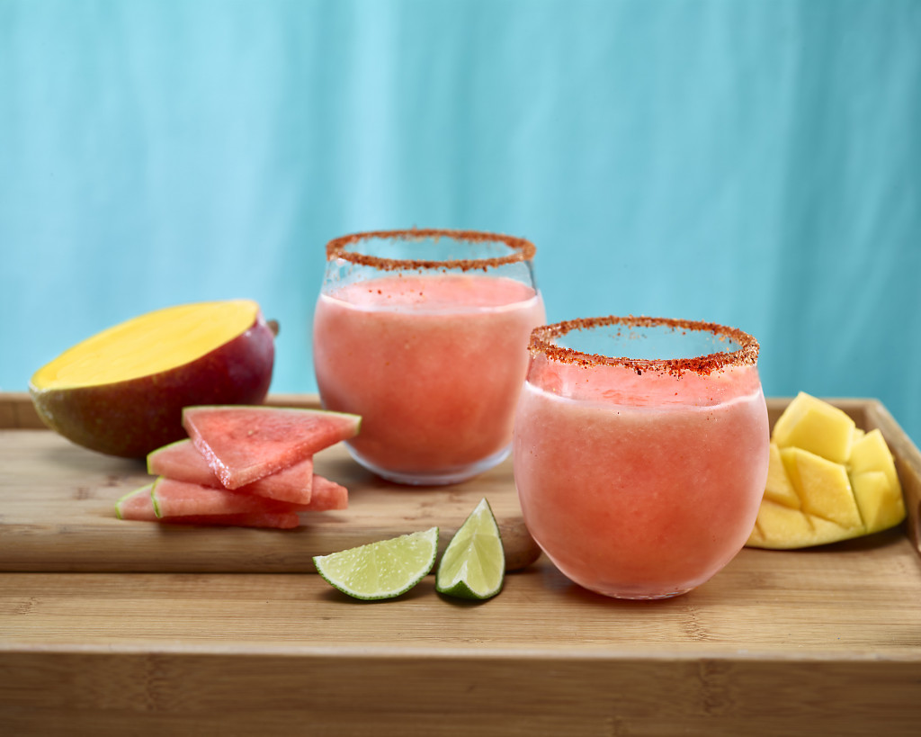 Watermelon Mango Margaritas in Tajin spice rimmed glasses. Garnishes of watermelon, mango and lime.