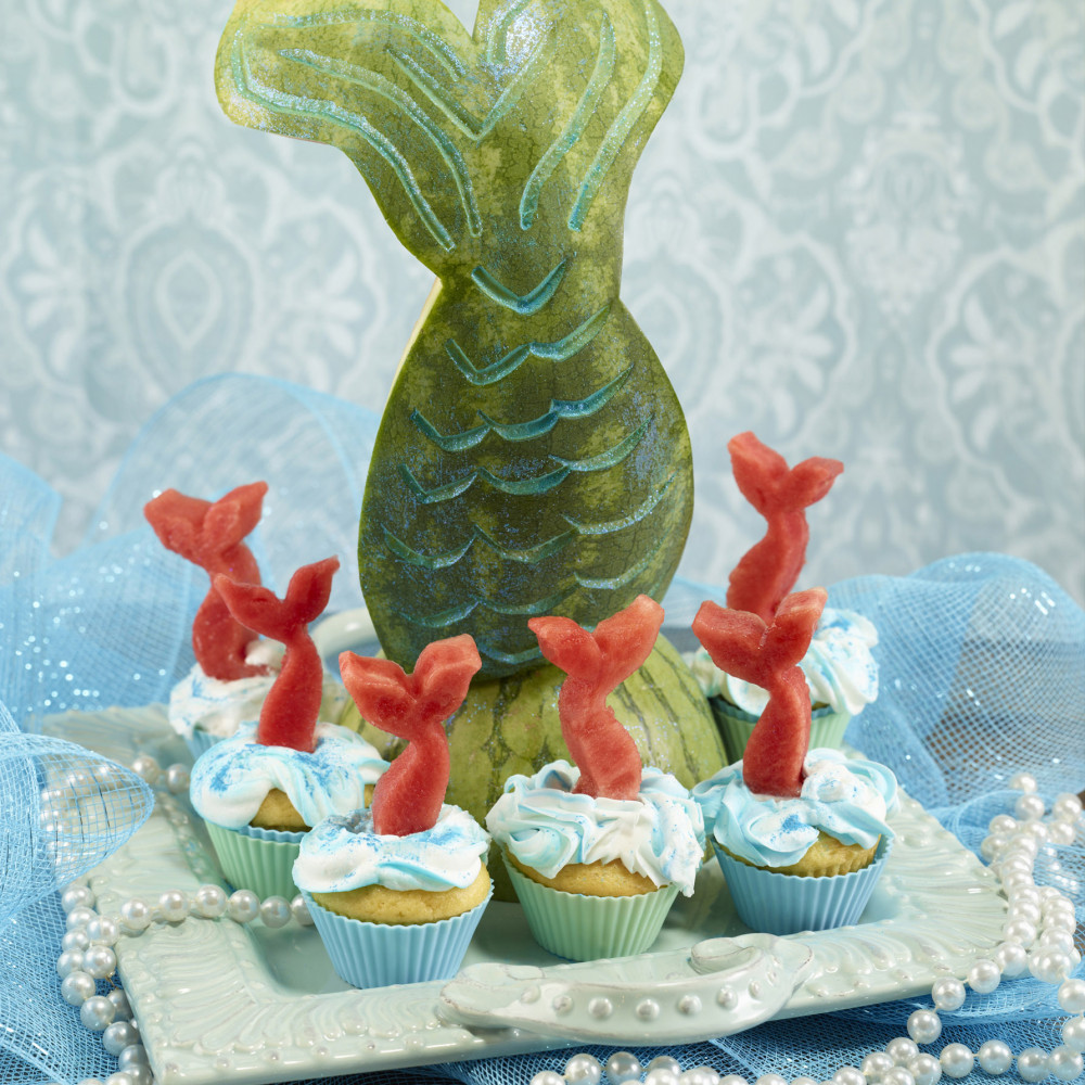 Watermelon carved as a mermaid tail with small cupcakes around it