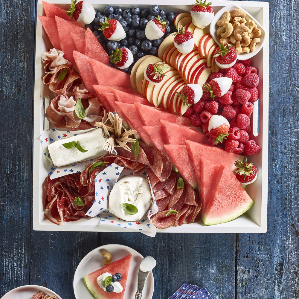 Patriotic Board Charcuterie set in square serving tray (triangular cut watermelon slices, raspberries, strawberries, blueberries, nuts, cheese, deli meats set on blue painted table