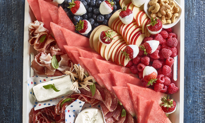 Patriotic Board Charcuterie set in square serving tray (triangular cut watermelon slices, raspberries, strawberries, blueberries, nuts, cheese, deli meats set on blue painted table