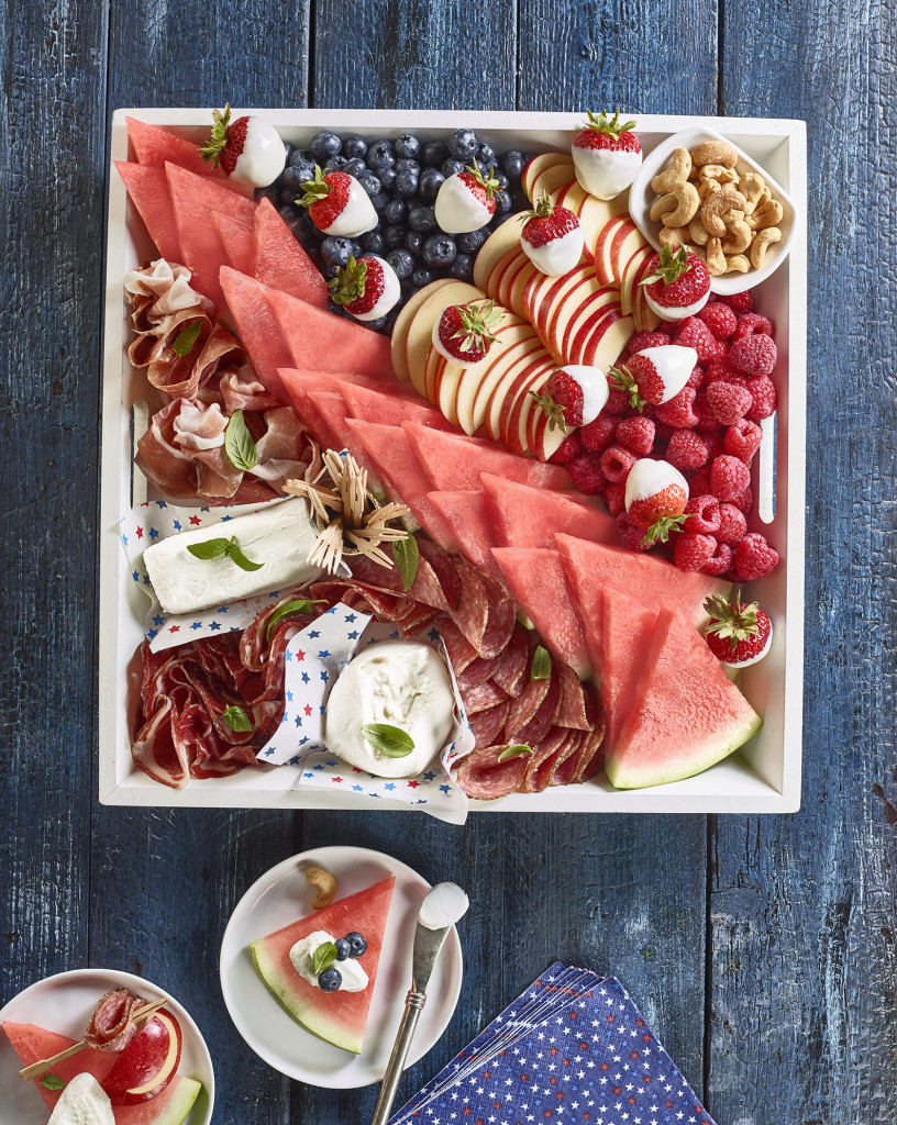 Patriotic Board Charcuterie set in square serving tray (triangular cut watermelon slices, raspberries, strawberries, blueberries, nuts, cheese, deli meats set on blue painted table