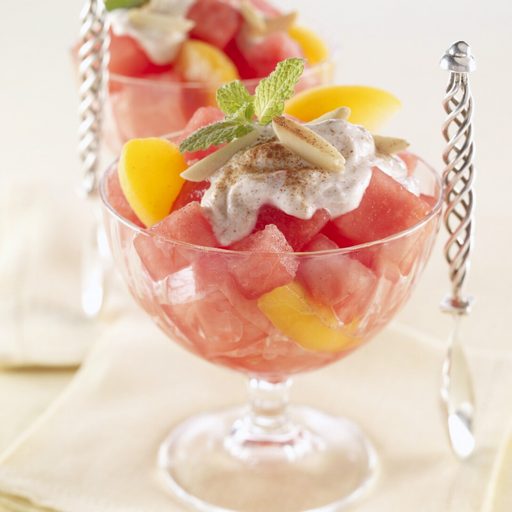 Two clear dessert dishes with watermelon peaches dessert topped with yogurt, slivered almonds, ground cinnamon and mint.