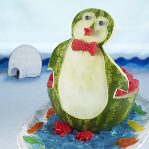 Penguin set on oval platter with blue gelatin cubes and watermelon cubes at base.