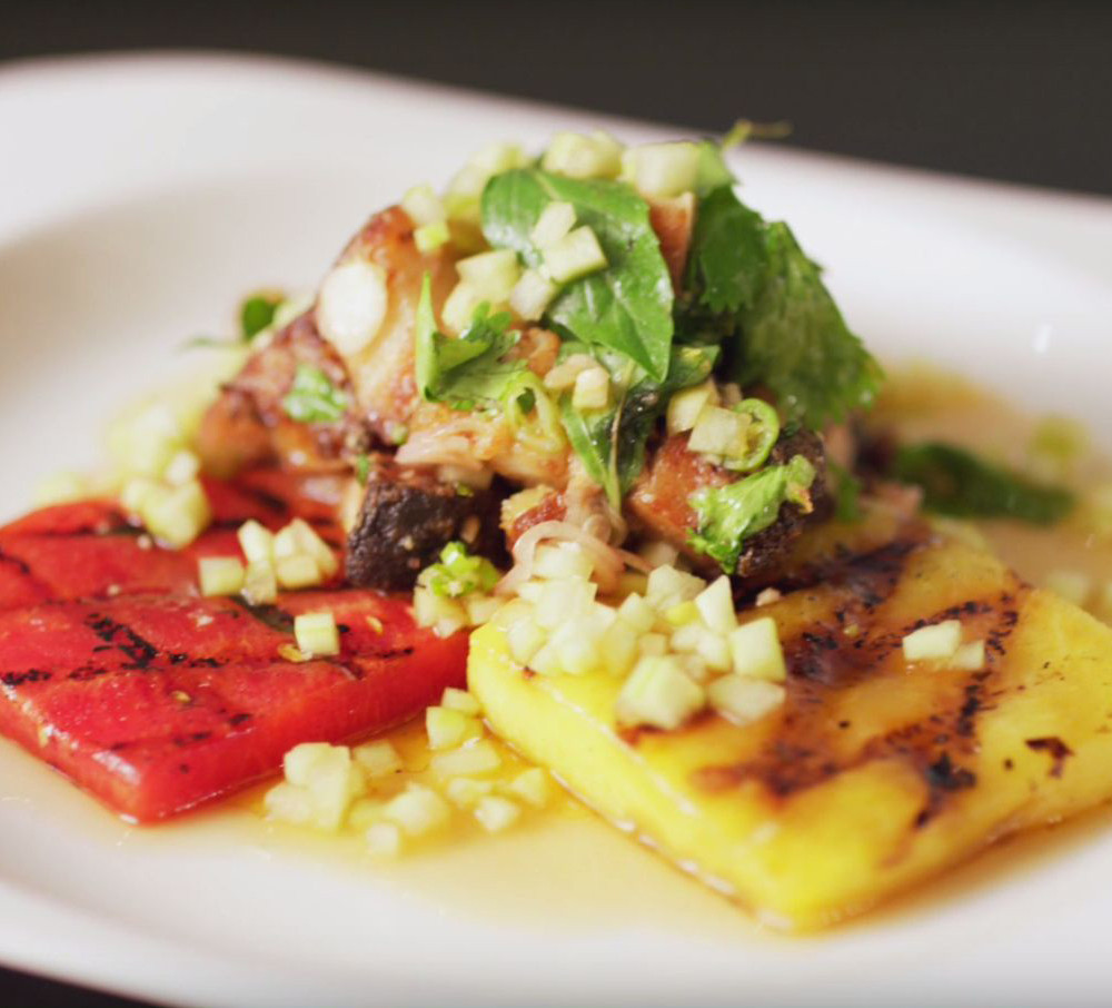 Red and Yellow watermelon as base with other stacked ingredients on white plate on black countertop.