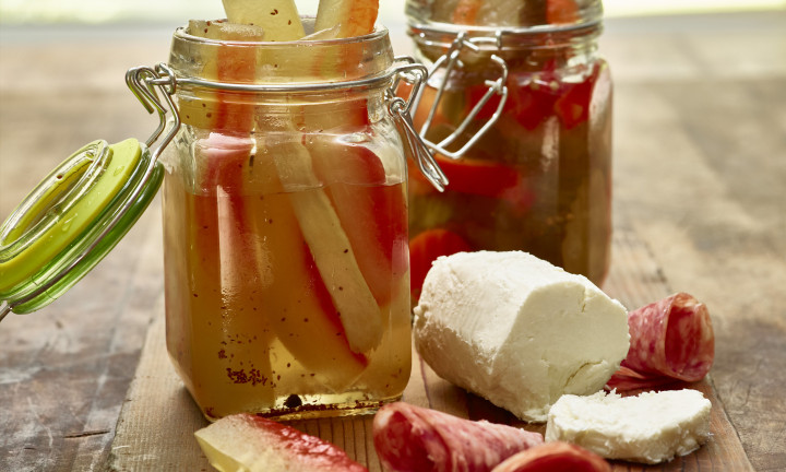 Watermleon rind pickles in two glass canister/jars, pictured with goat cheese and deli meats on wooden cutting board