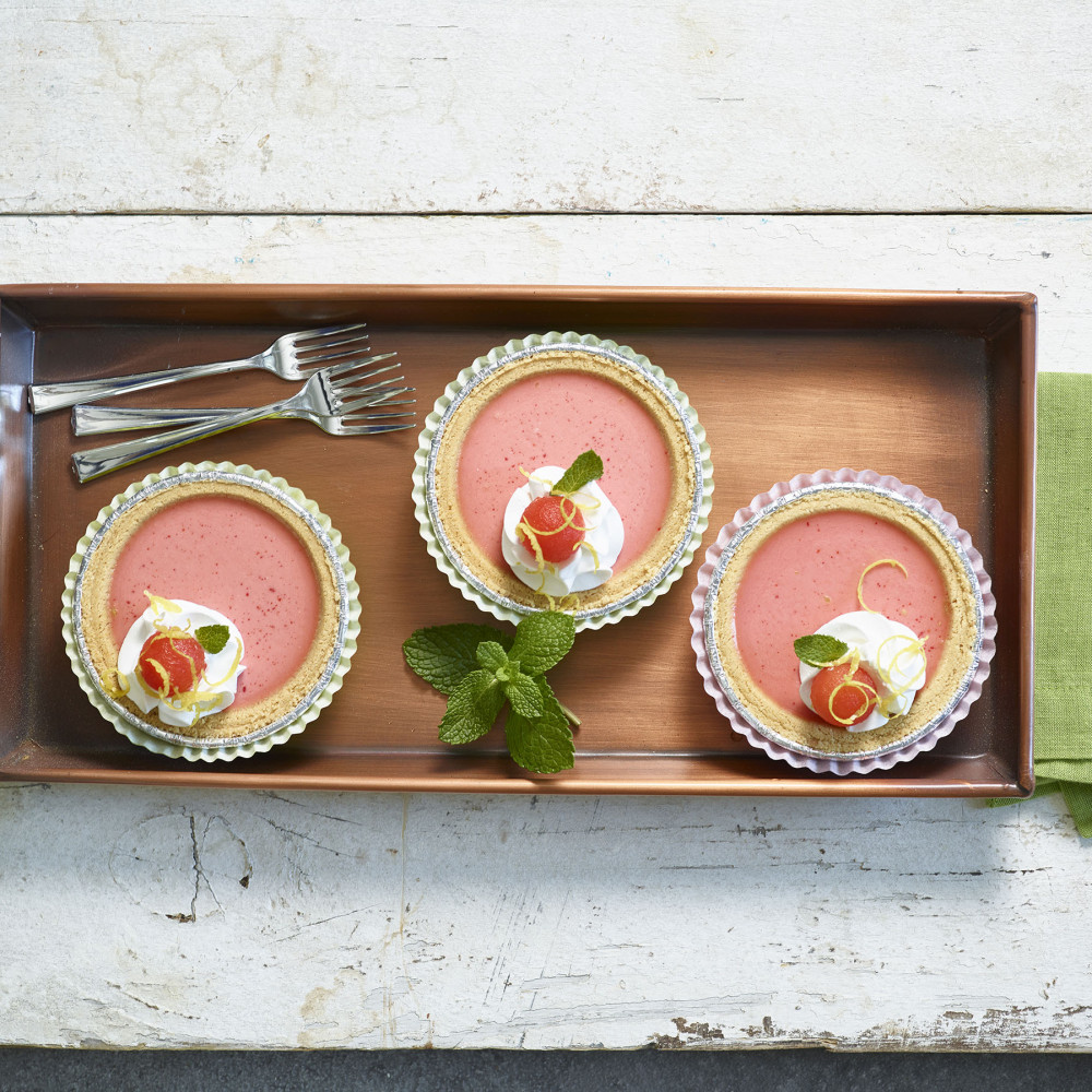 Three Watermelon Pies served on a wooden serving tray with mint, whipped cream, lemon zest and watermelon ball as garnishes.