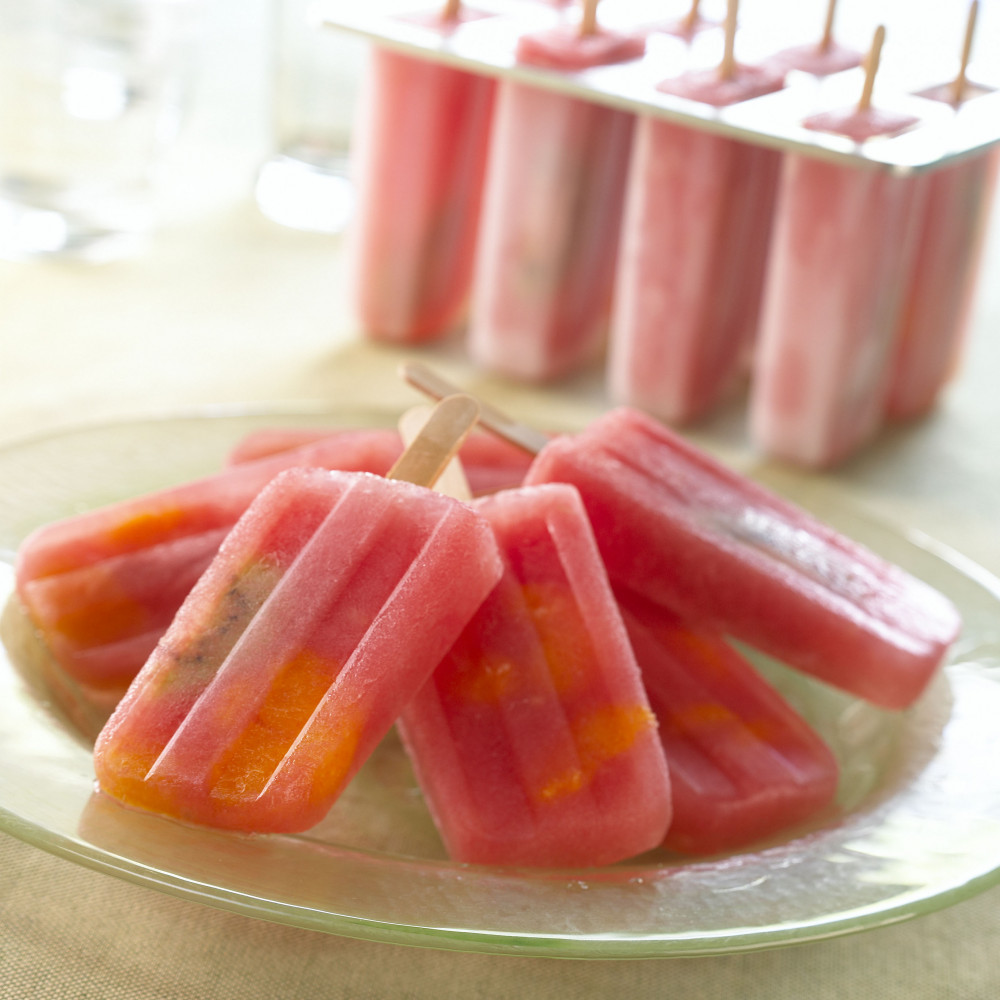 Watermelon popsicles fanned-out on a plate with popsicles in popsicle tray in background.
