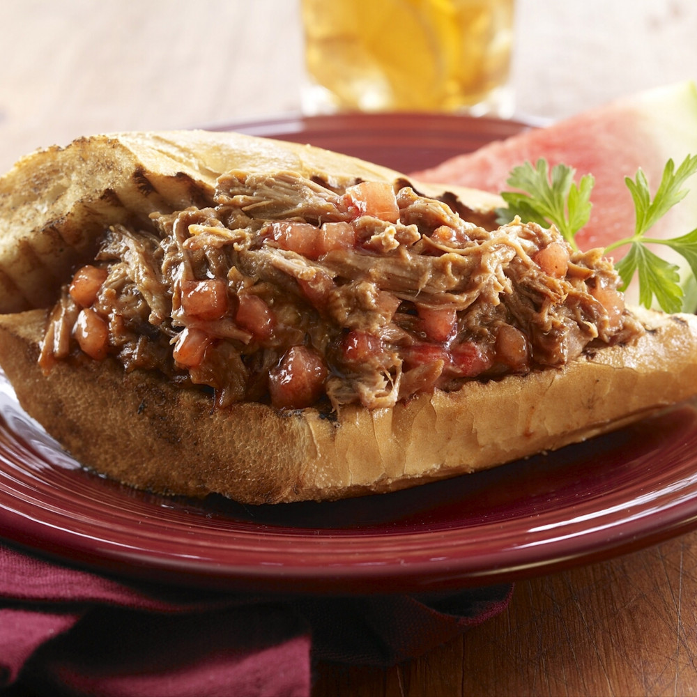 Open-faced sandwich on grilled bread on a red stoneware plate with red napkin. Clear beer mug in background.