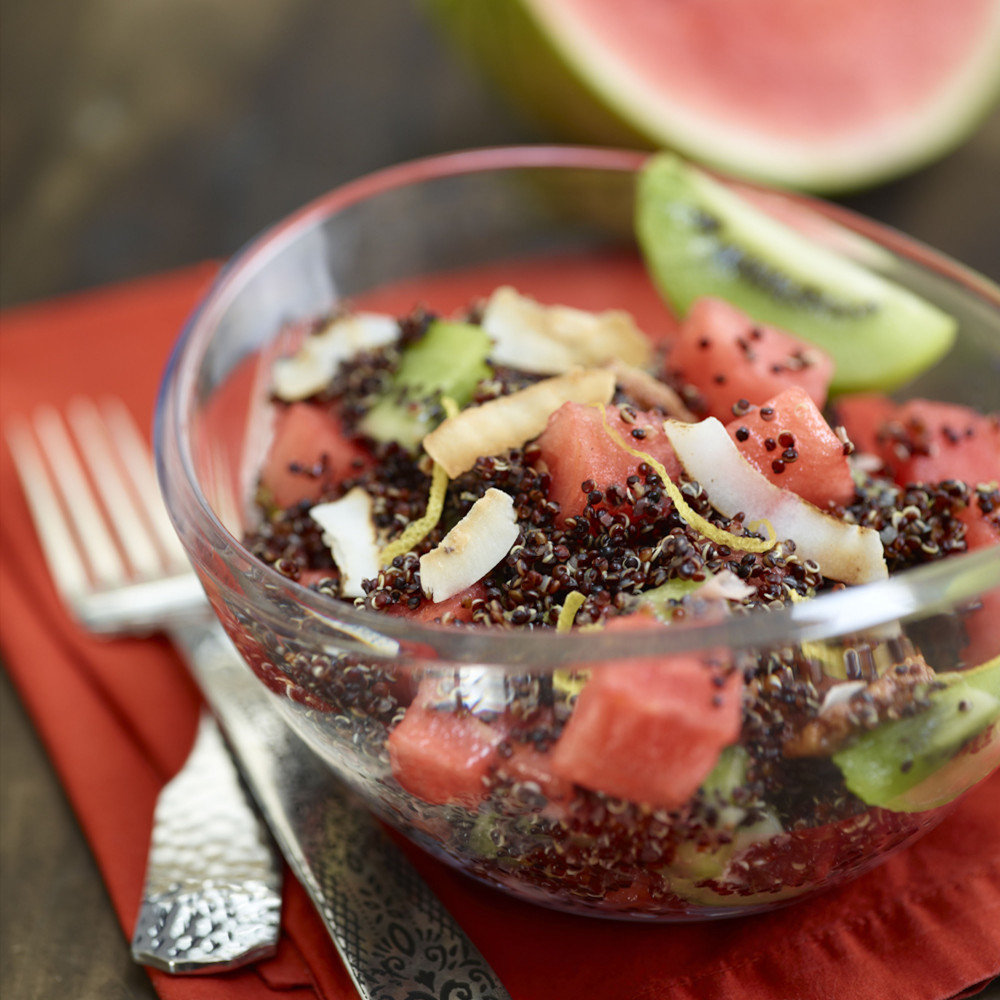 Quinoa Salad in clear bowl atop red napkin with two forks on side, watermelon wedge in background.