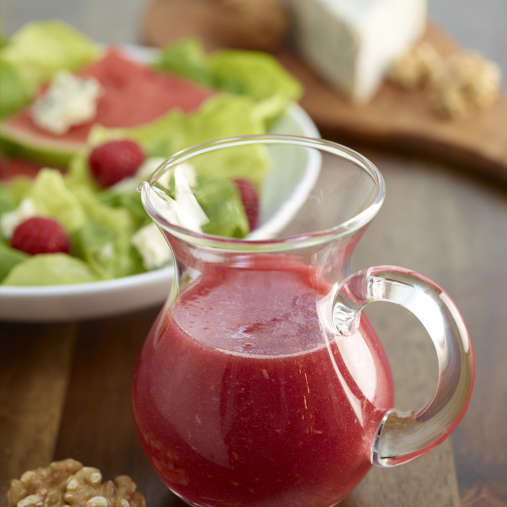 clear miniature pitch of vinaigrette on side of salad, also walnuts, cheese wedge and bread