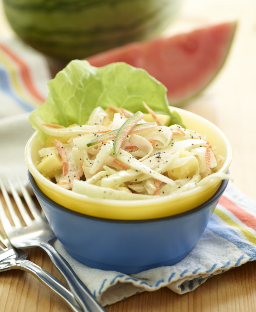 watermelon rind slaw in stacked blue and yellow bowls with leaf of lettuce, forks and whole and wedge of watermelon in background on wooden board with folded kitchen towel