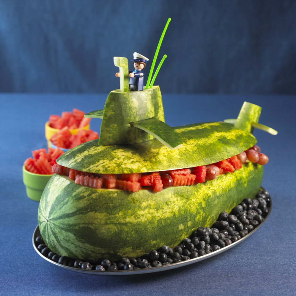 Submarine set on large oval platter with blueberries at base. Toy Captain set on top.