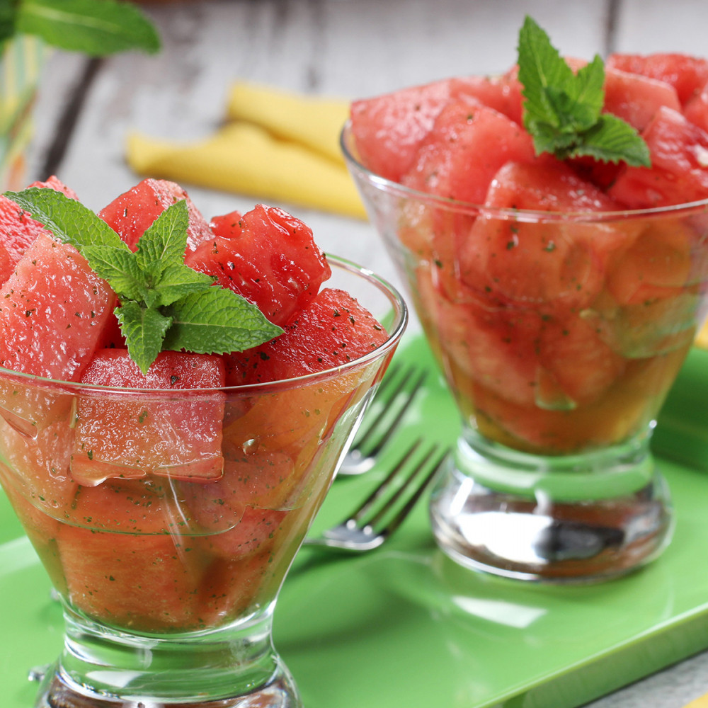 watermelon mojito salad in two clear dessert glasses atop a green serving tray with sprigs of mint and two forks