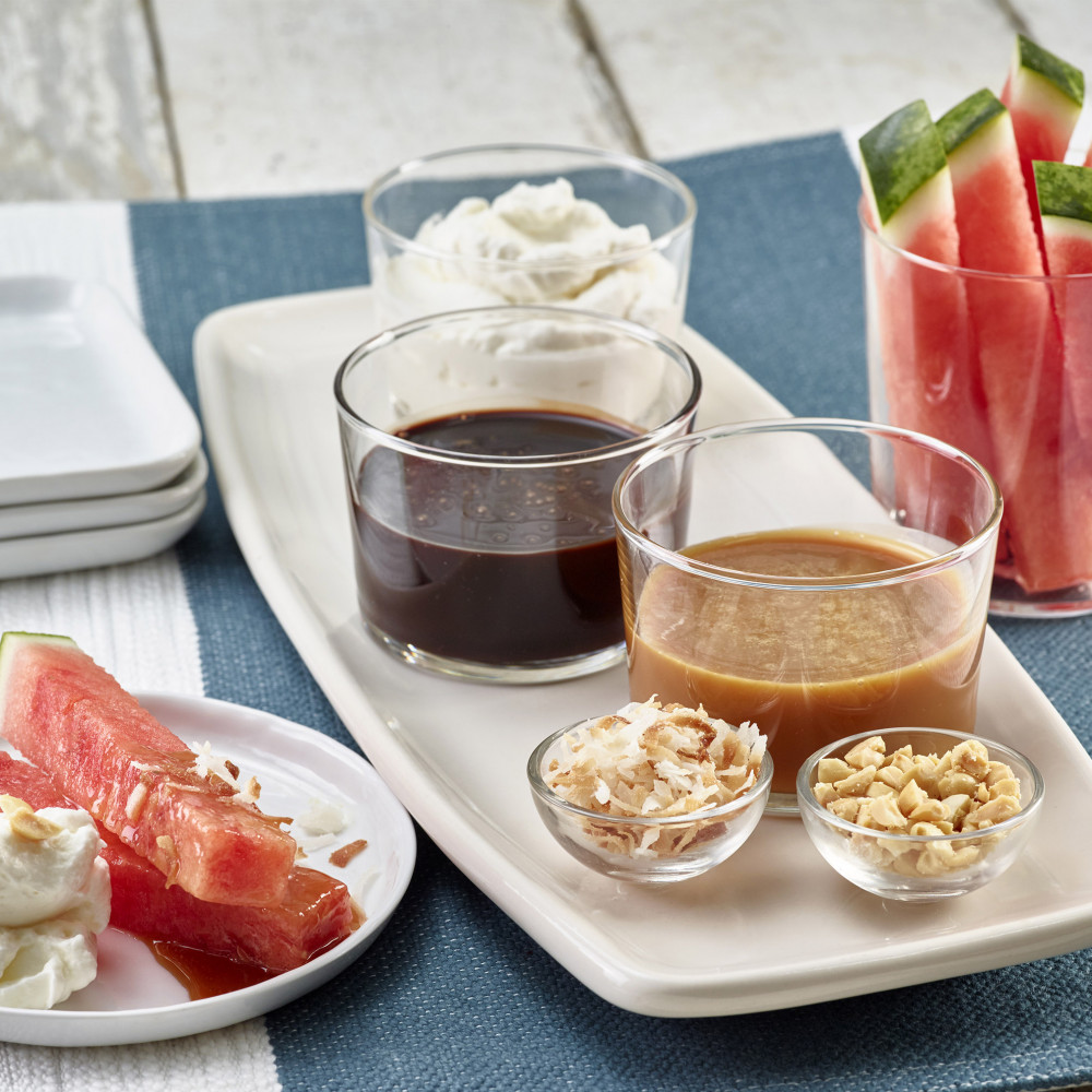 Watermelon Dippers (watermelon stix with rind) served with liquid chocolate, caramel, whipped cream, crushed nuts and toasted coconut with dessert plates on side.
