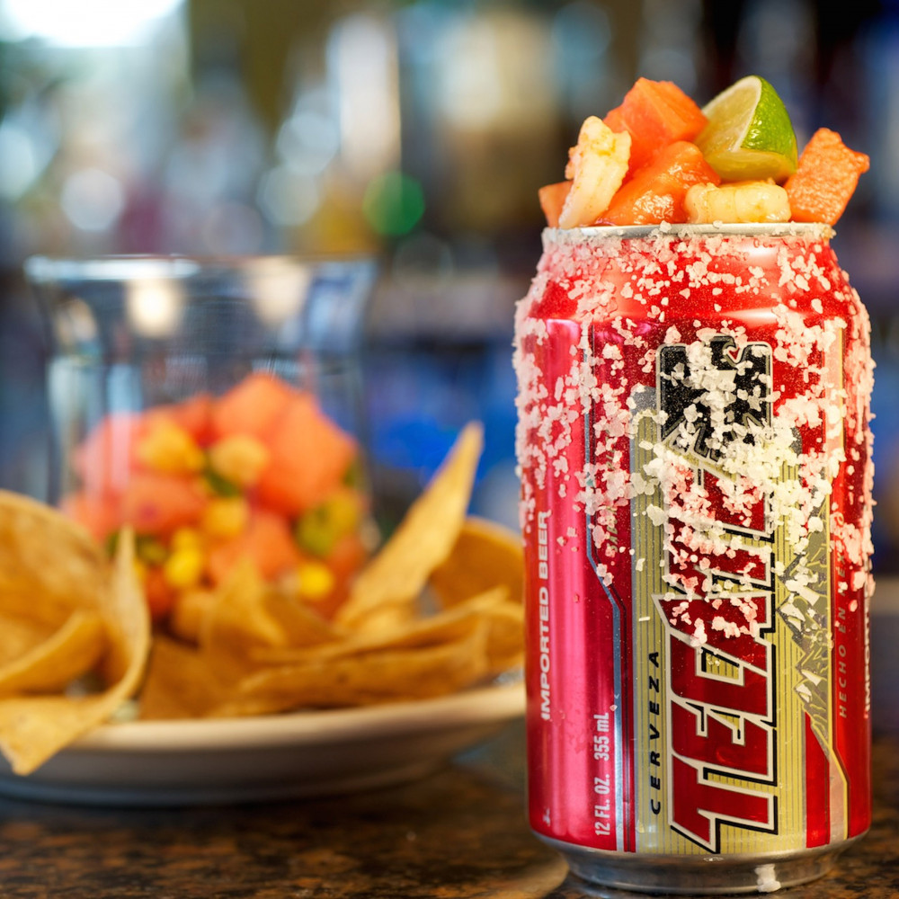 Can of Tecate beer topped with Ceviche. Ceviche and chips in background.