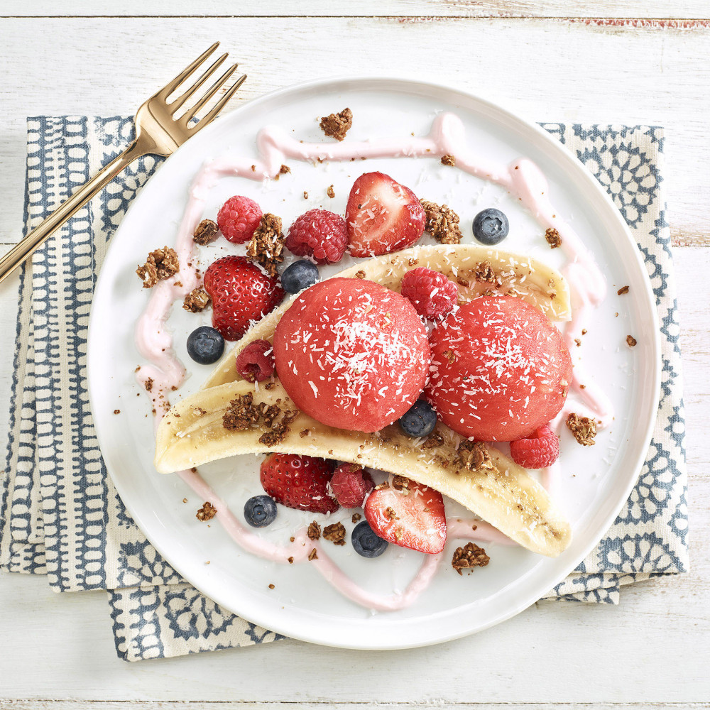 Overhead view of a watermelon breakfast banana split with scooped watermelon and toppings