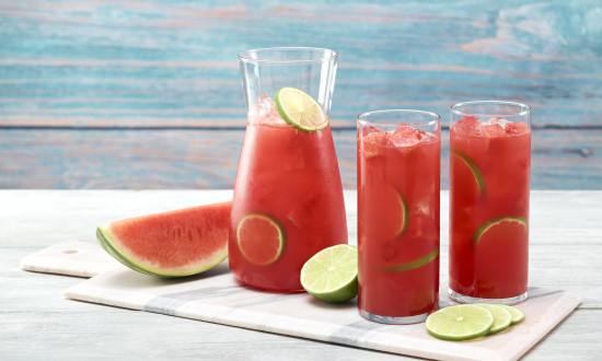 Two glasses of watermelon limeade with pitcher on marble