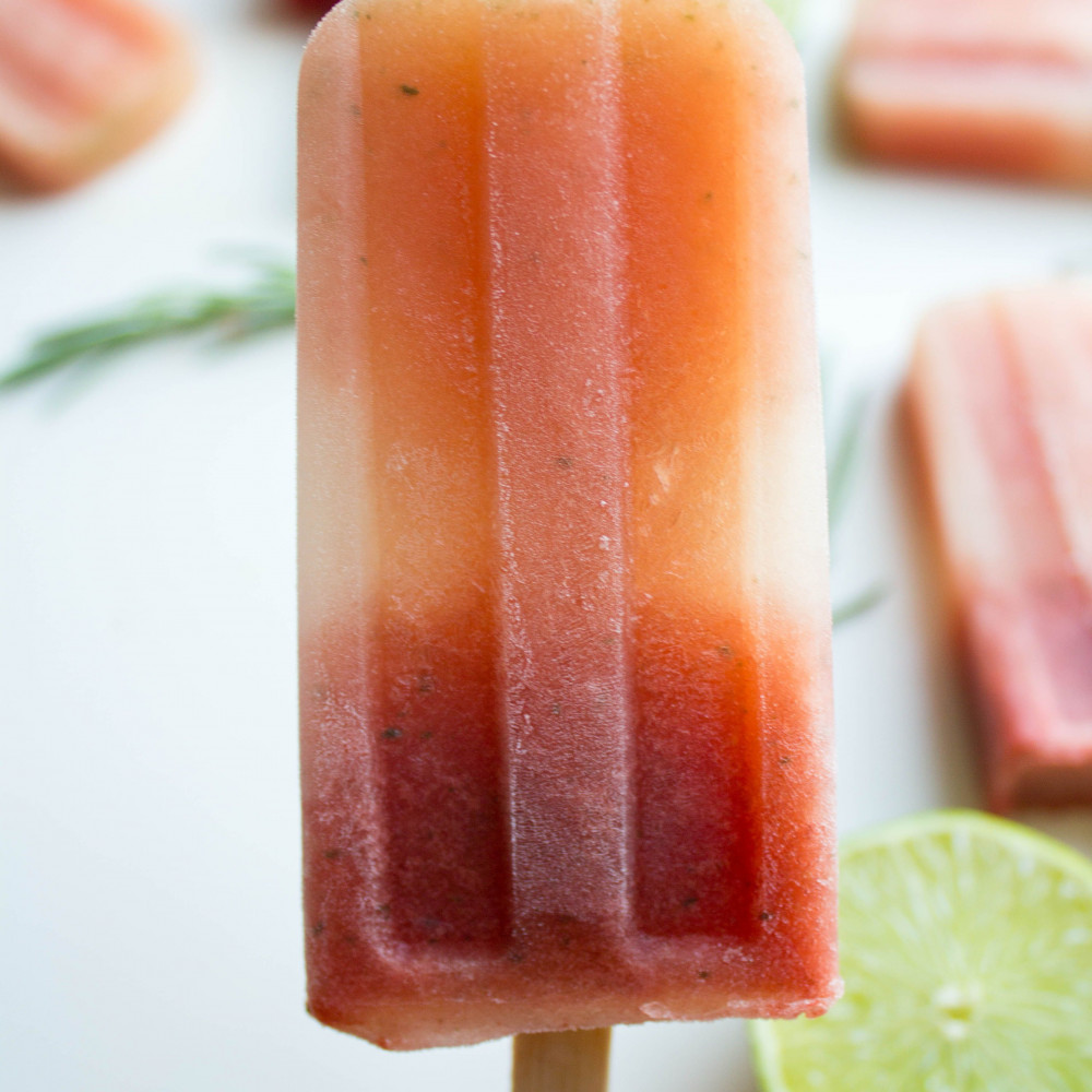 handheld popsicle with lime and rosemary in background with more popsicles