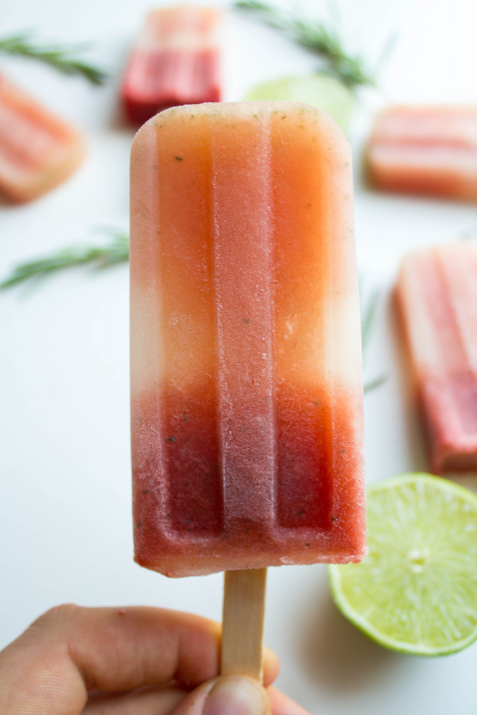 handheld popsicle with lime and rosemary in background with more popsicles