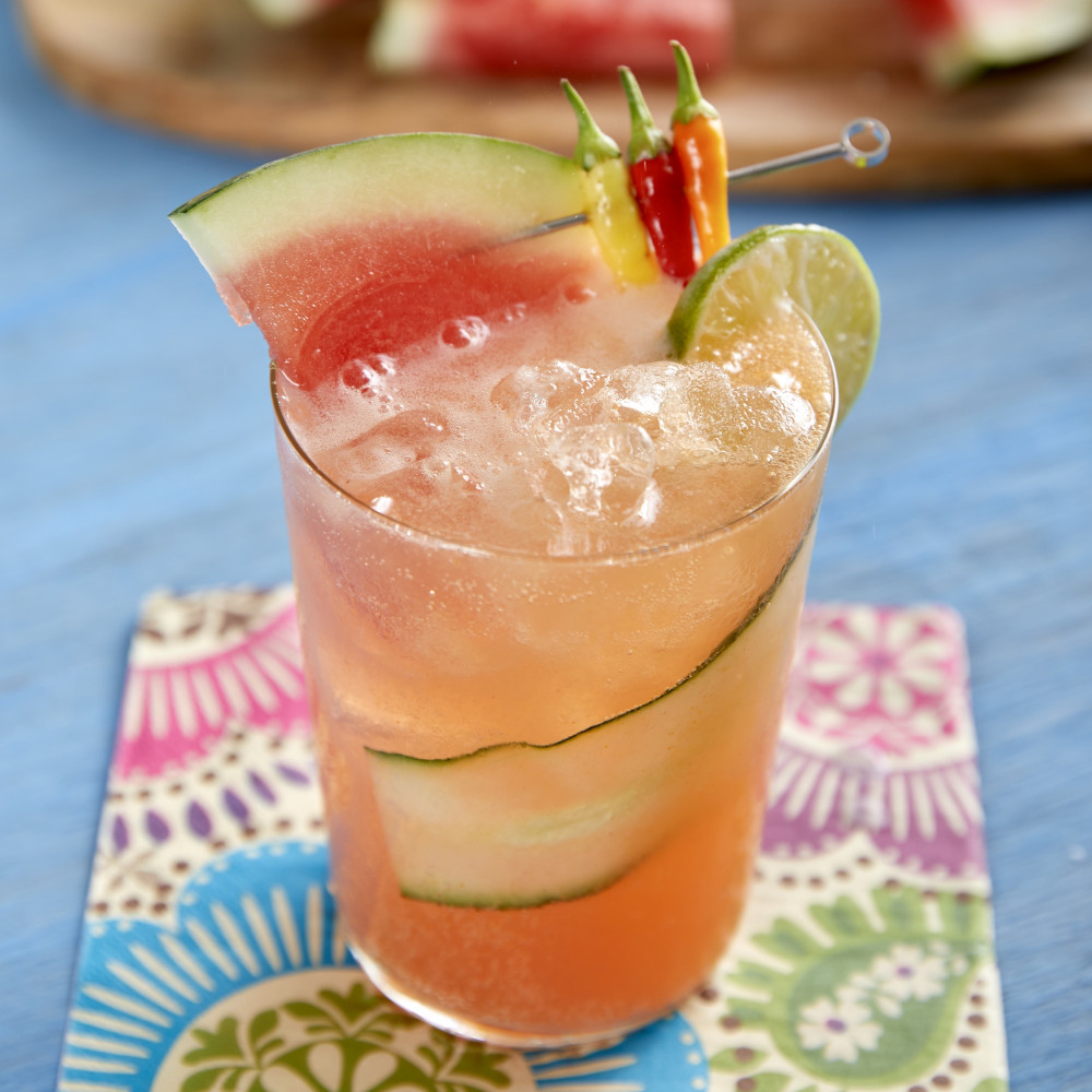 Spicy Watermelon Agua Fresca served in tall/collins glass garnished with watermelon, lime wheel, cucumber ribbon, peppers