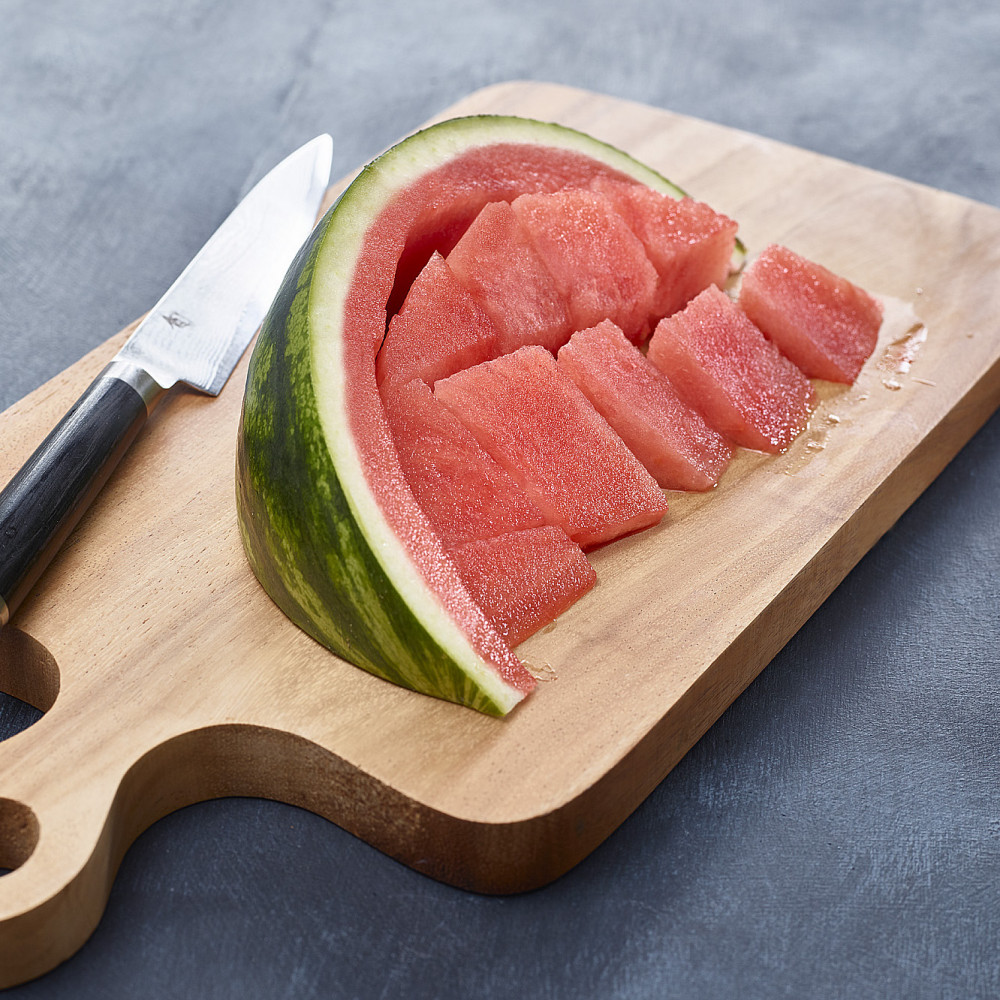 Watermelon wedges cut from rind on cutting board with knife