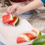 person placing watermelon wedges on white platter