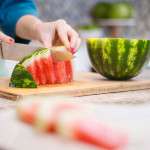 person slicing watermelon wedges on cutting board