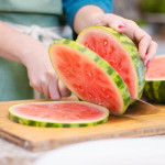 person slicing watermelon rounds on cutting board