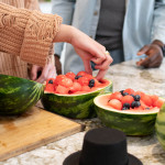 watermelon shells with watermelon balls, person picking from shell/bowl