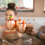 three people in hot tub toasting mule mugs with watermelon garnish