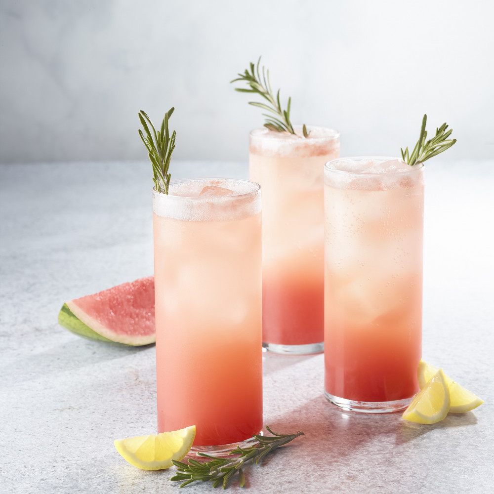 Three watermelon rosemary lemonade soda drinks in highball glasses with ice.