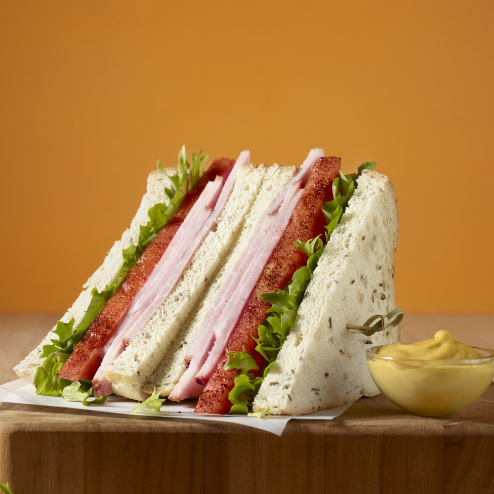 Ham, watermelon slice and lettuce on rice bread with mustard on cutting board.