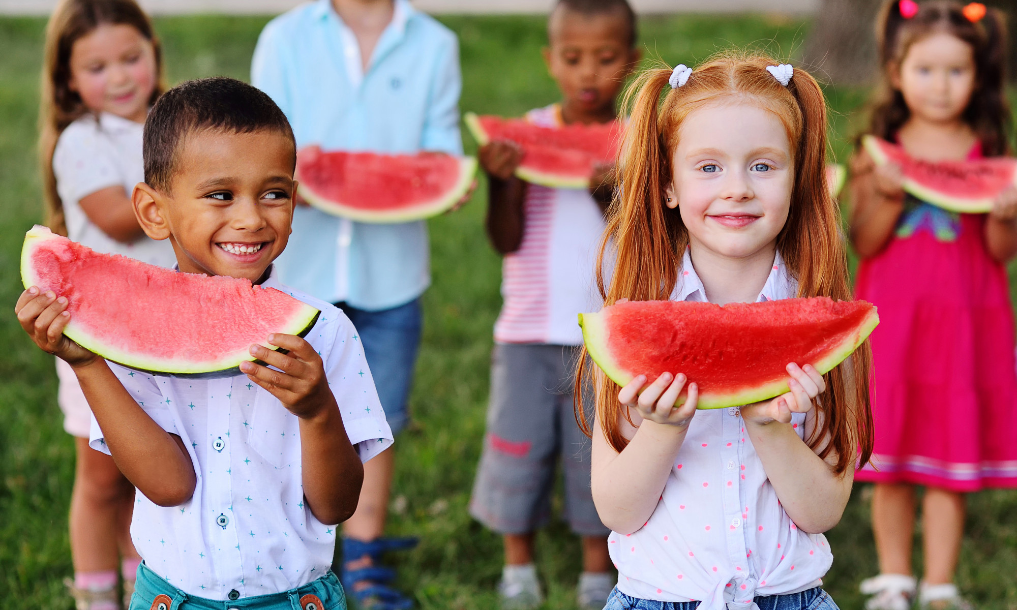 group of happy preschool children of different ethnic types are holding slices of ripe watermelon and smiling at the background of the Park on a Sunny summer day.