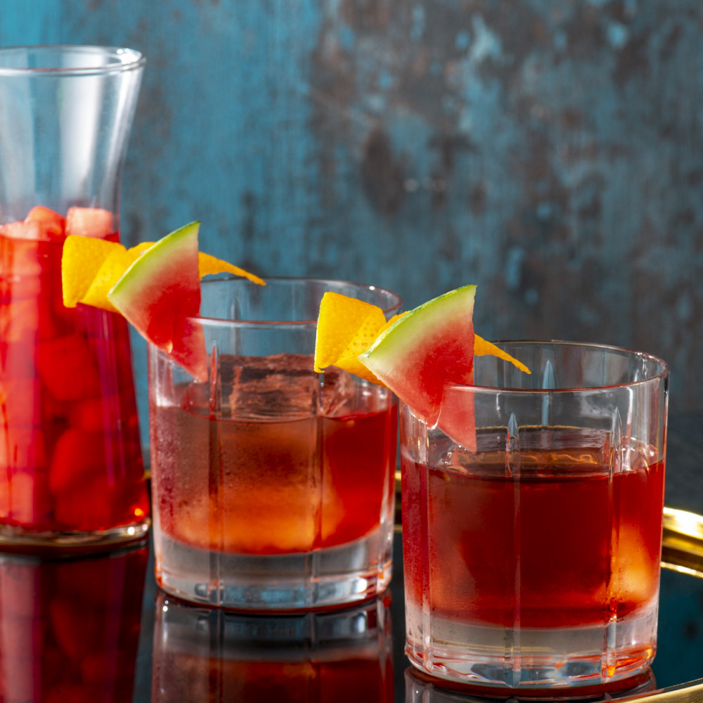 Two prepared negronis with watermelon campari infusion in pitcher in background