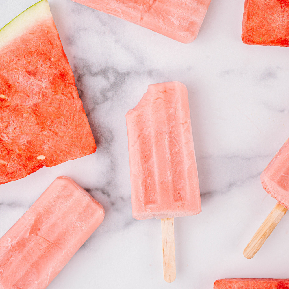 Watermelon yogurt popsicles with watermelon wedges on a marble board