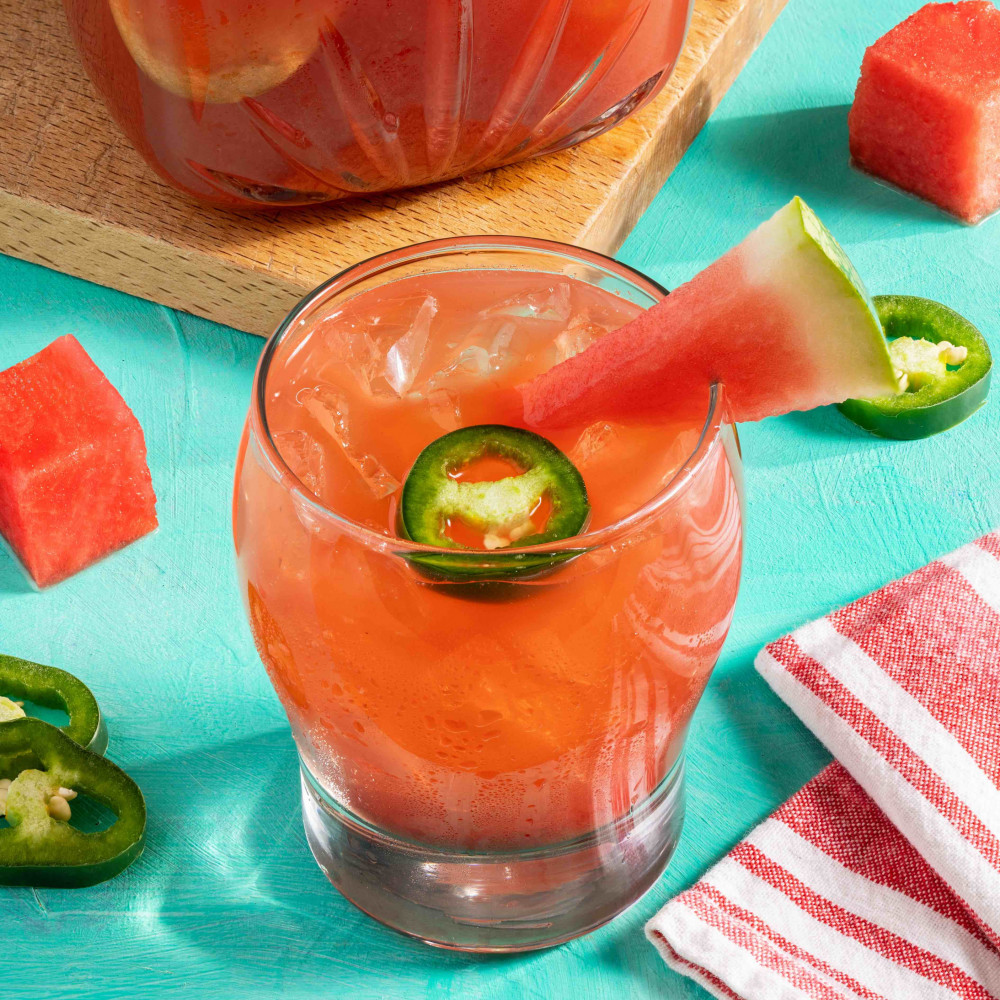 Cup of watermelon agua fresca with jalapeno and watermelon wedge along with a pitcher of the juice