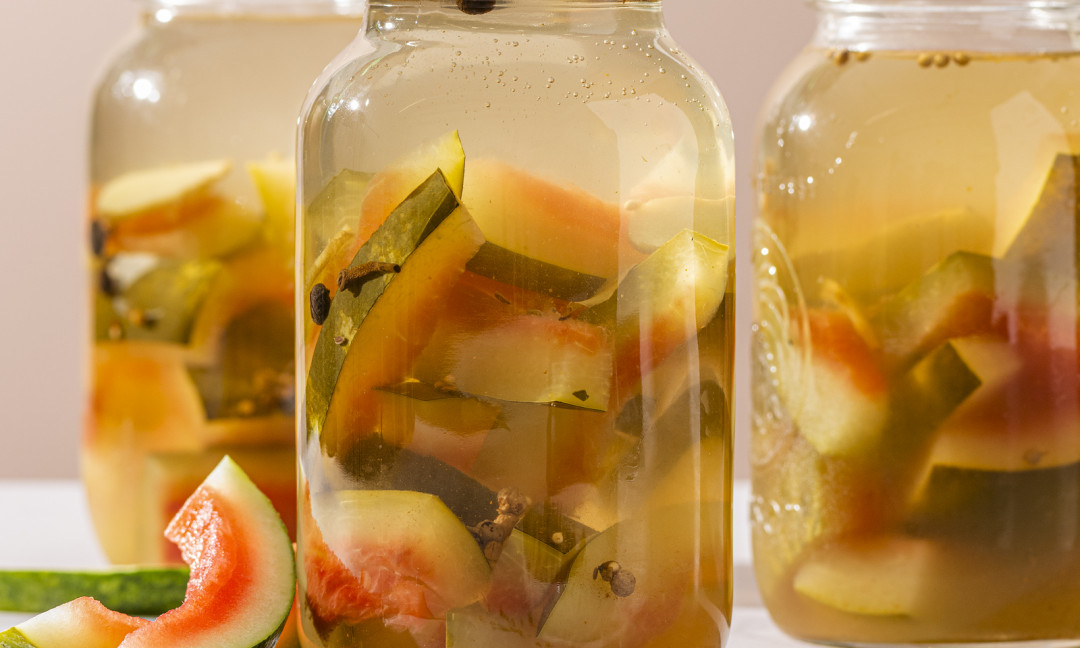 Three jars of pickles made with watermelon rind and small bowl of spices