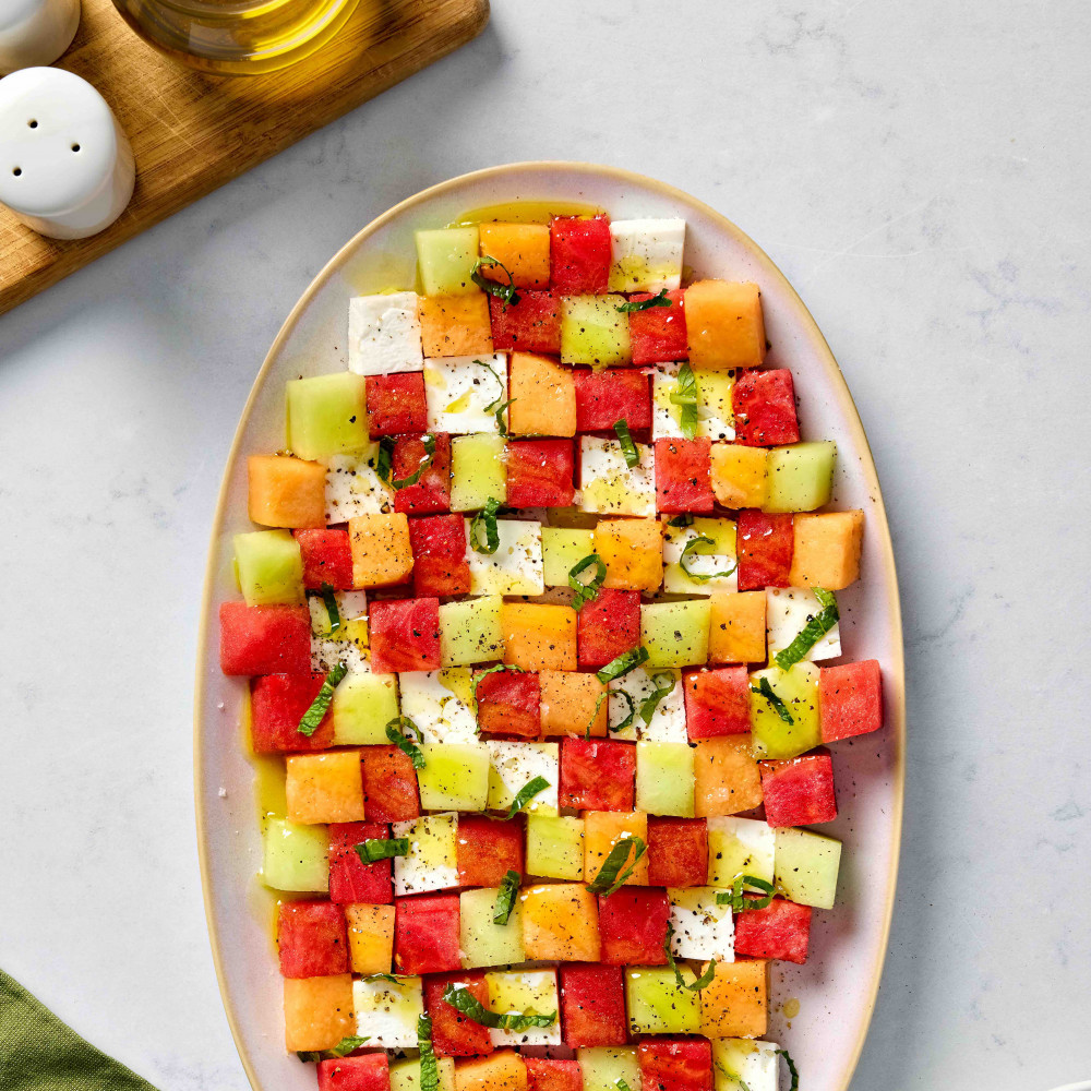 Watermelon, cantaloupe, honeydew and feta are all cut in similar cube shapes and arranged on a platter with olive oil drizzle and mint.