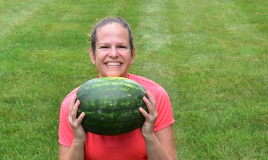 Smiling girl in a squat stance holding a watermelon