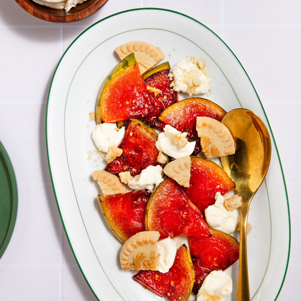 Bruleed and carmelized watermelon wedges with cookies and creme fraiche on a white oval plate with gold serving spoon