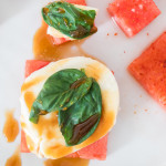 Watermelon caprese flavor pairing including sliced watermelon, mozzarella, basil and balsamic on a white plate