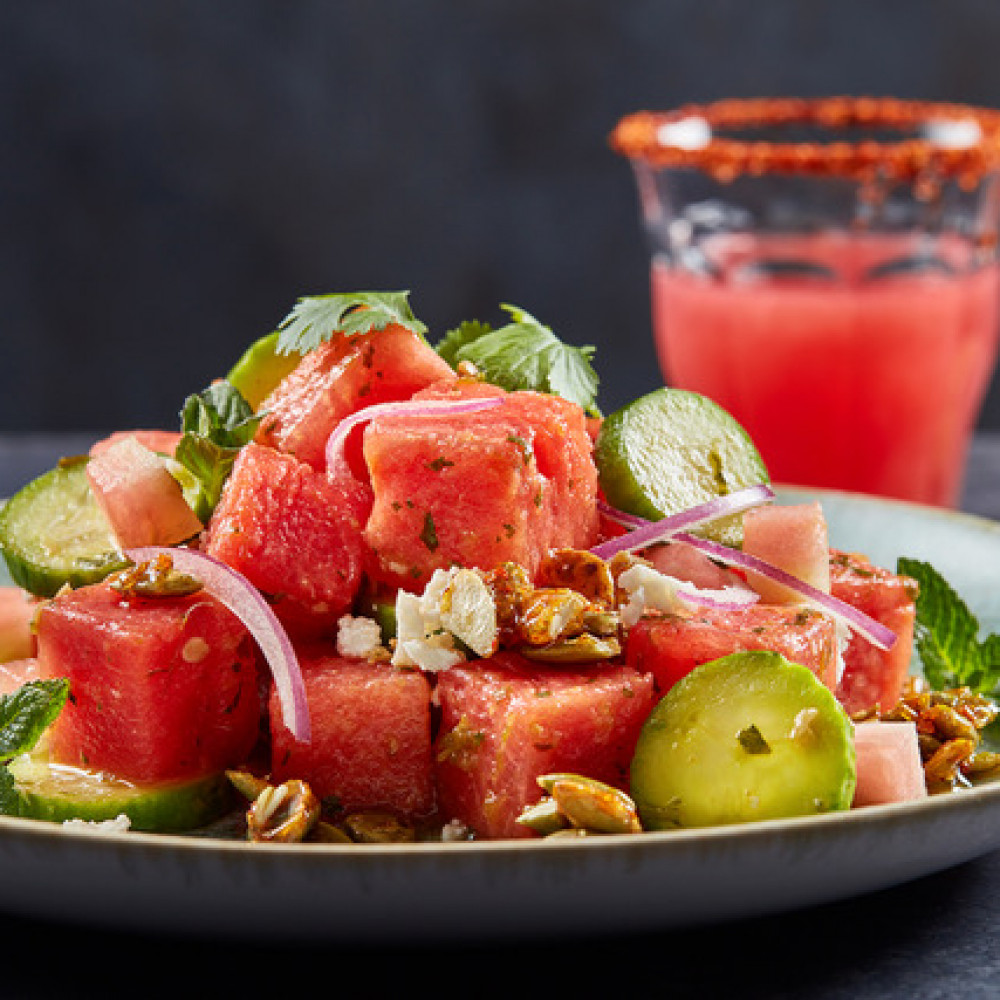 Smoked watermelon Salad on a plate with watermelon margarita and lime wedge in the background.