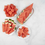 four different cuts of watermelon in white bowls - cubes, sticks, wedges and cut out stars. All on grey marble background