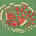 different cuts of watermelon and watermelon rind in the shape of a oblong watermelon on a green background