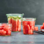 three different cuts of watermelon - sticks, cubes and balls in clear glass containers on a grey background.
